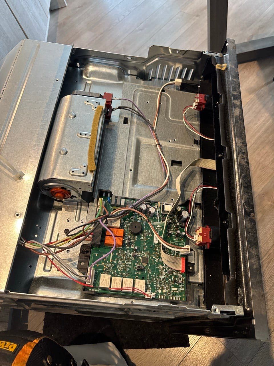 Appliance repair in Toronto — control assembly removed from a built-in appliance, showing the board, relays, terminal blocks and a cooling blower