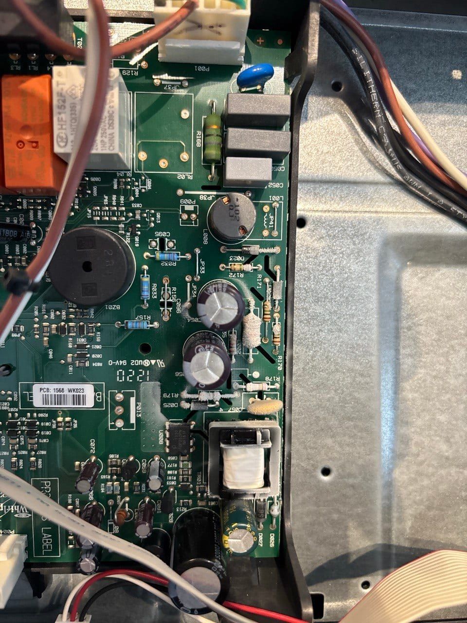 Appliance repair in Toronto — control board with relays, capacitors and a transformer inside the metal chassis, wiring harnesses entering from the left
