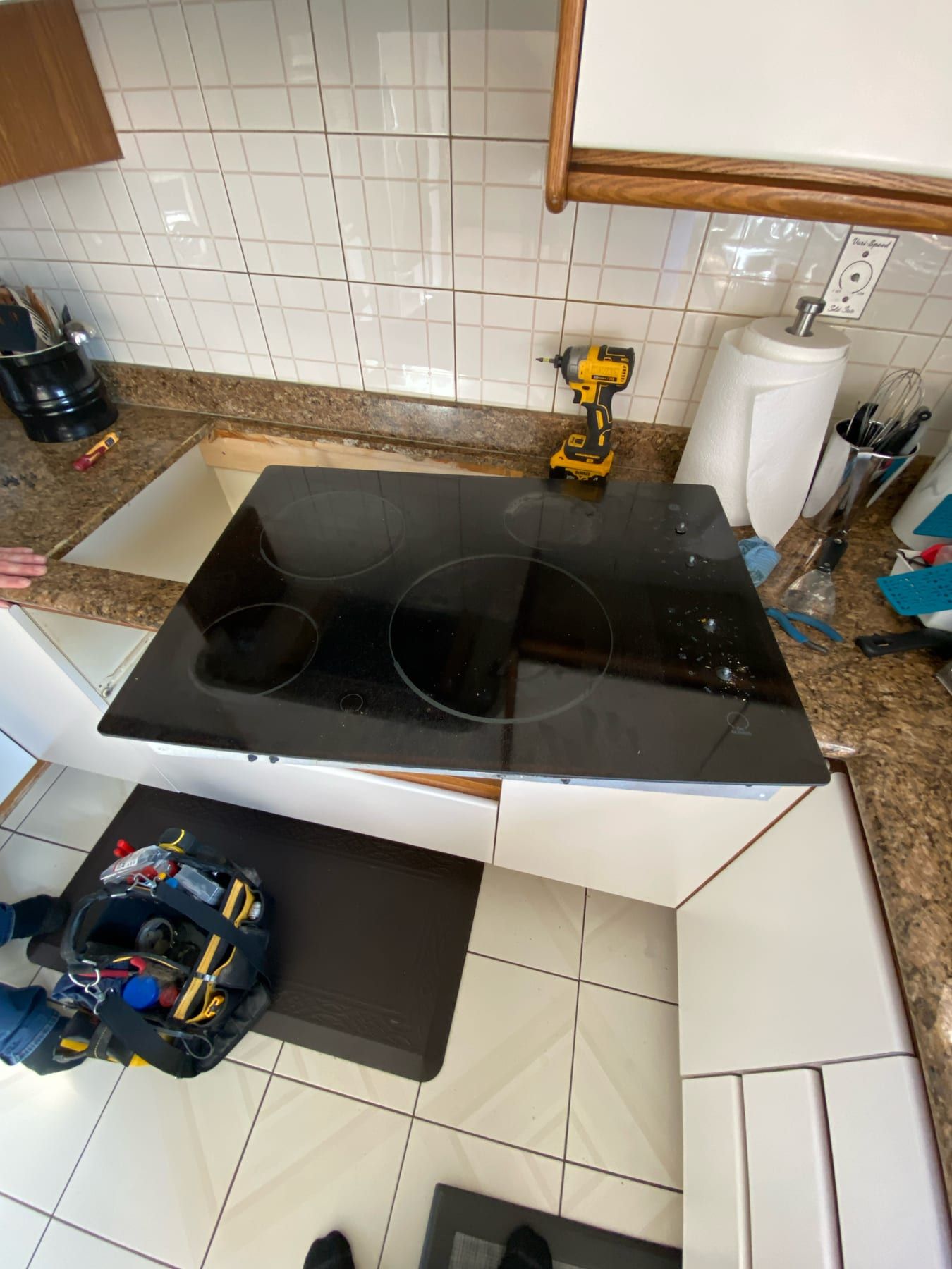Cooktop installation in Toronto — black ceramic cooktop resting over the countertop cutout with a wooden support strip and a cordless drill beside it
