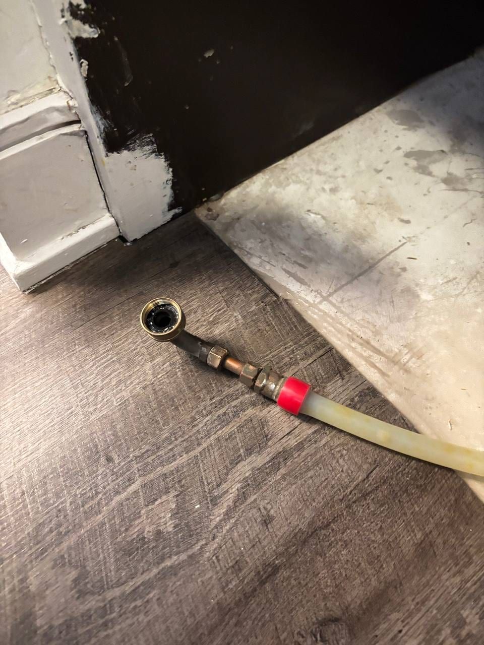 Appliance installation in Toronto — disconnected water supply line with a brass compression fitting, adapters and plastic tubing on a wooden floor