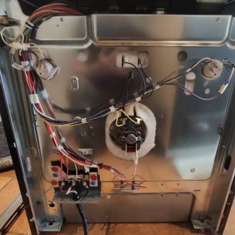 Range repair in Toronto — rear cover removed showing the four-terminal block with red, black, white and green wires, the convection fan motor and two thermostats
