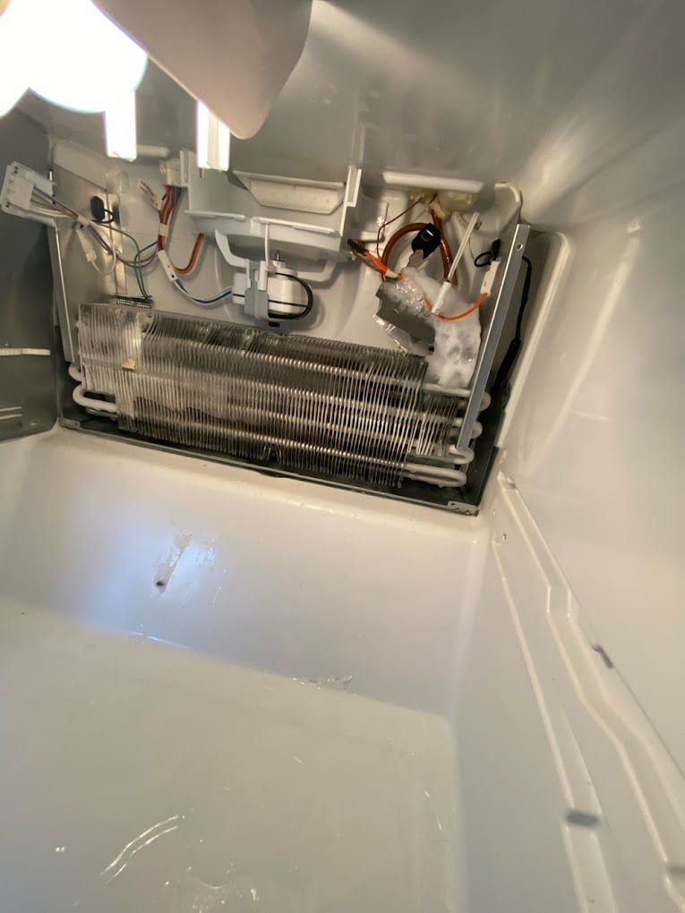 Freezer repair in Toronto — rear panel removed inside the freezer showing the evaporator coil, defrost heater, sensor and ice on the wall