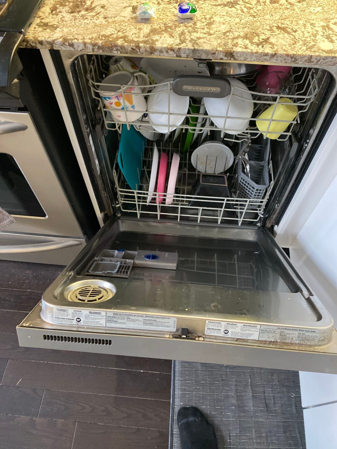 KitchenAid dishwasher repair in Toronto — built-in dishwasher with the door open, both racks loaded, cycle labels and the detergent dispenser on the door