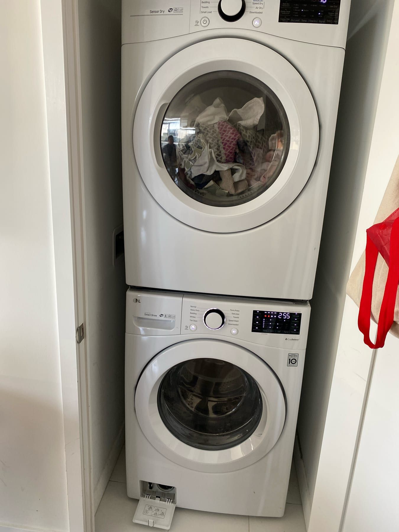 LG washer repair in Toronto — LG stacked washer and dryer with the washer display lit and the drain filter door open, hose pulled out