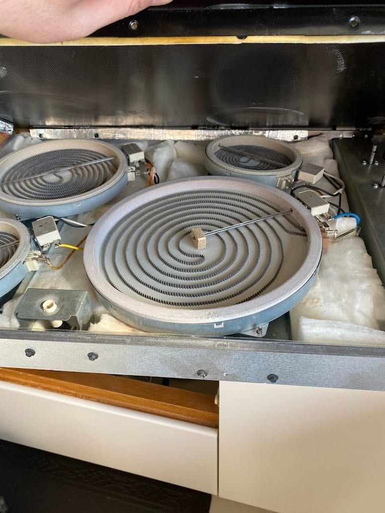 Cooktop repair in Toronto — glass surface lifted on its hinges showing four radiant heating elements, temperature limiters and wiring
