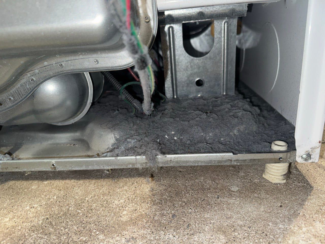 Dryer repair in Toronto — front panel removed showing the blower housing, wiring and a thick layer of grey lint on the base of the machine