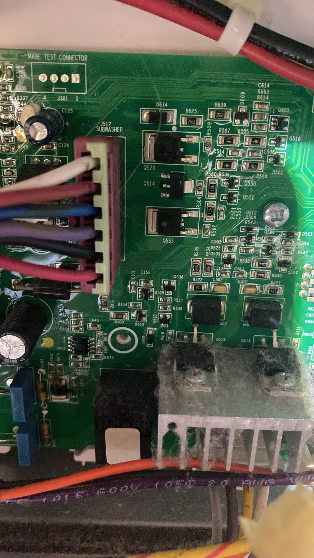 Washer repair in Toronto — close-up of a control board with a plugged wiring harness, power transistors on a heatsink and dust across the components